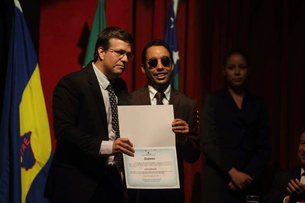 O vereador Lucas Aribé está recebendo seu diploma das mãos do promotor da 2ª Zona Eleitoral, Henrique Ribeiro Cardoso.