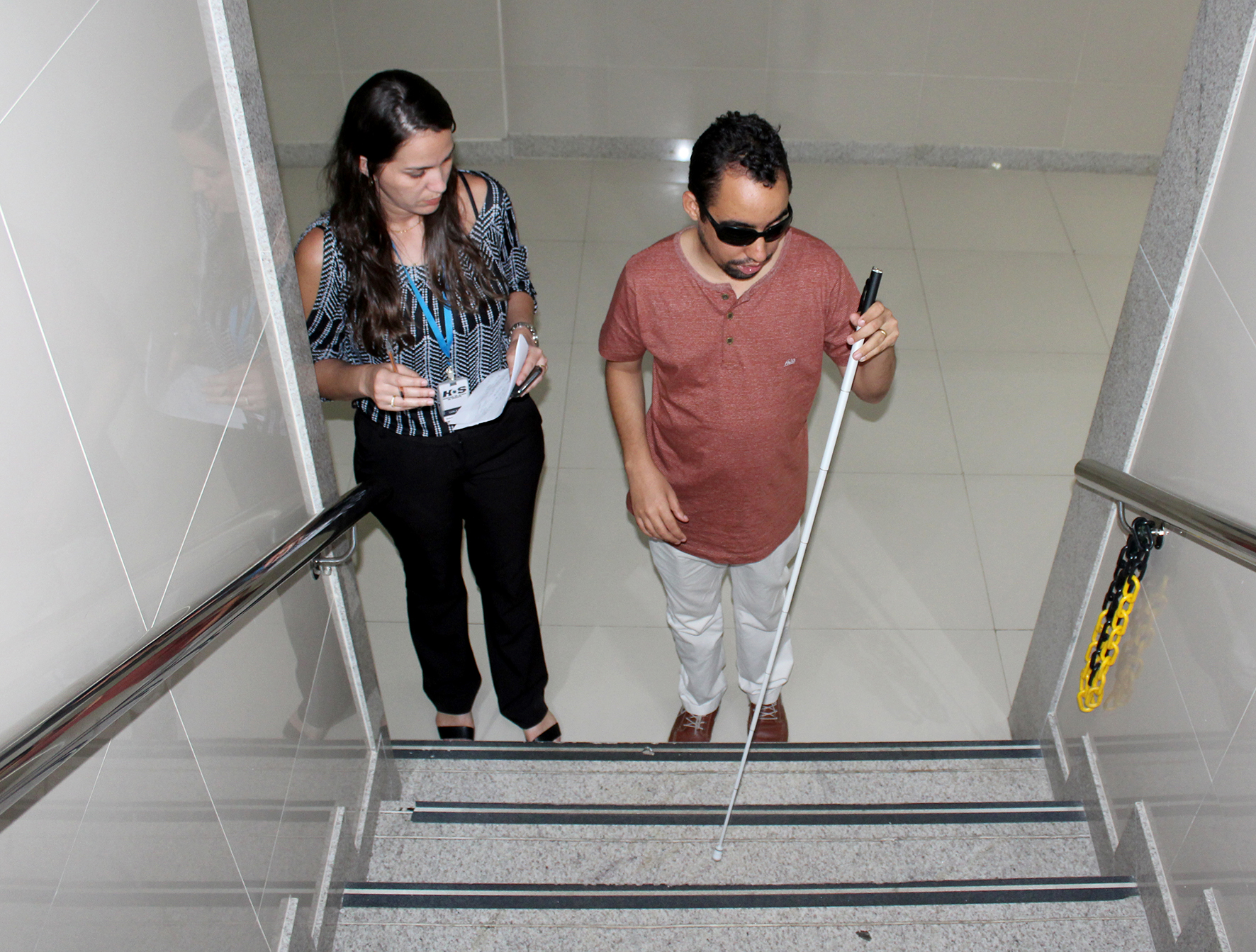 #PraCegoVer: Lucas observa situação da escada do prédio, acompanhado da gerente de Marketing, Carla Rego