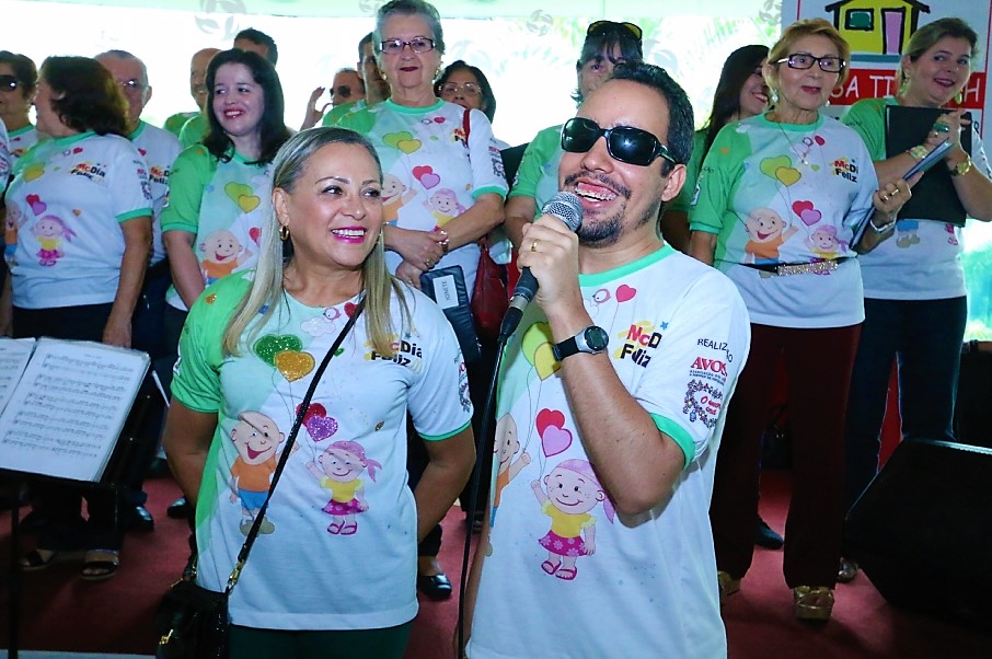 #PraCegoVer - Lucas canta ao lado de voluntárias (Foto: Acrisio Siqueira/Arquivo Avosos)