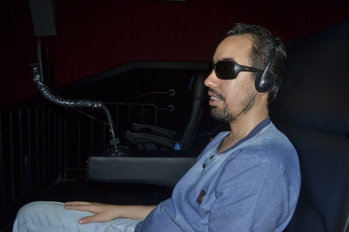 #PraTodoMundoVer Lucas Aribé na sala de cinema utilizando o equipamento para ouvir a audiodescrição