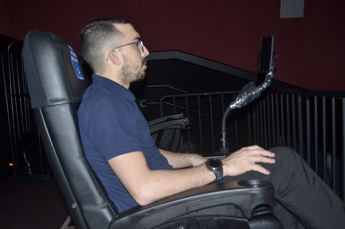#PraTodoMundoVer Pablo Ramon sentado na sala de cinema assistindo ao filme com o equipamento de Libras